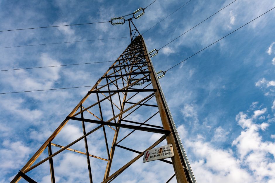 A detailed low-angle shot of a power line tower extending into a cloudy blue sky.