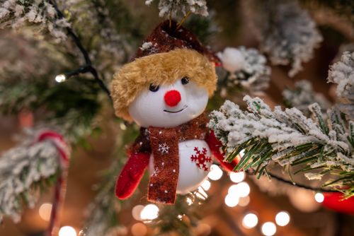 Free Close-up of a charming snowman ornament hanging on a snowy Christmas tree branch. Stock Photo