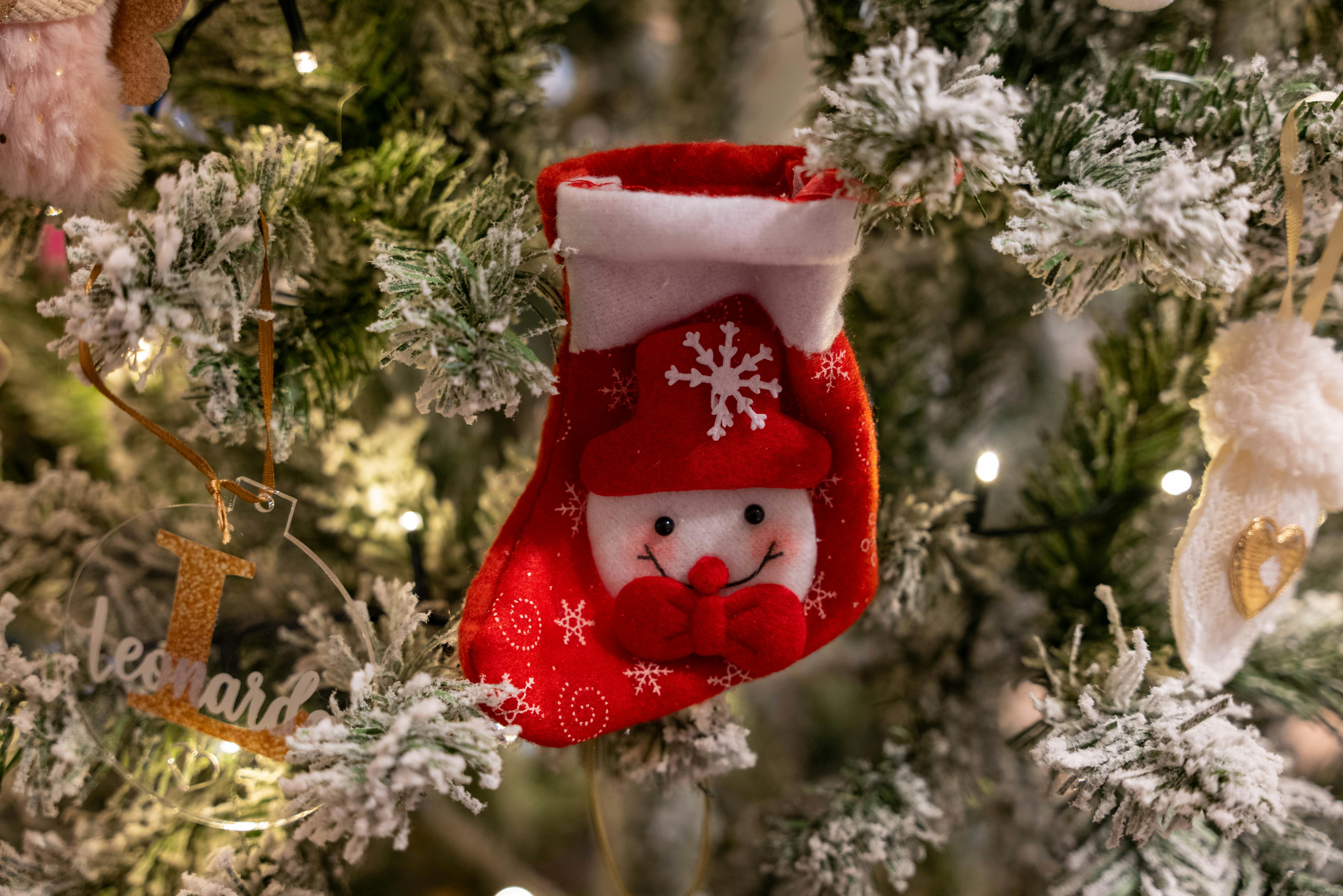 tags for christmas stockings - Close-up of a festive red stocking on a Christmas tree with lights and decorations.