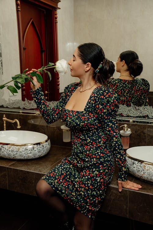 Woman in a Floral Dress Smelling a Flower