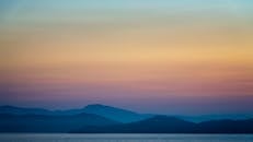 宁静的风景中，雾蒙蒙的山脉与平静海面上的日落被捕捉下来