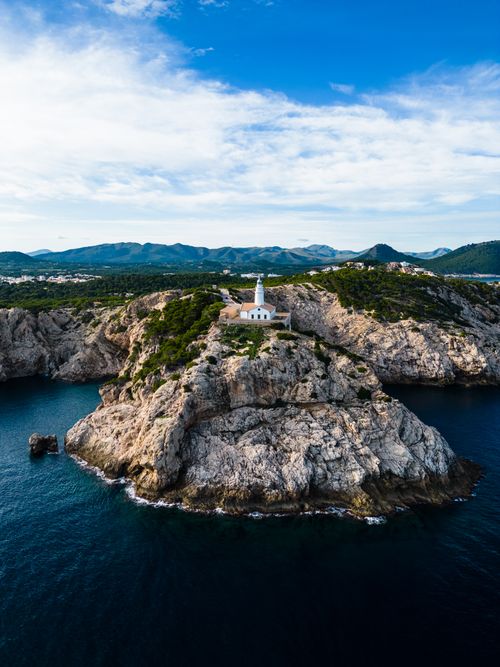 Free A breathtaking aerial view of a lighthouse perched on a rocky coastline surrounded by sea. Stock Photo