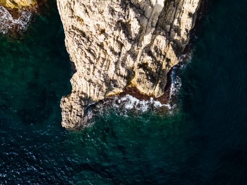 Free Drone shot showcasing a stunning rock formation against the vibrant turquoise ocean waves. Stock Photo