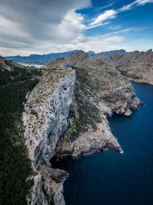 Free Aerial view of dramatic coastal cliffs meeting the blue sea under a vibrant sky. Stock Photo