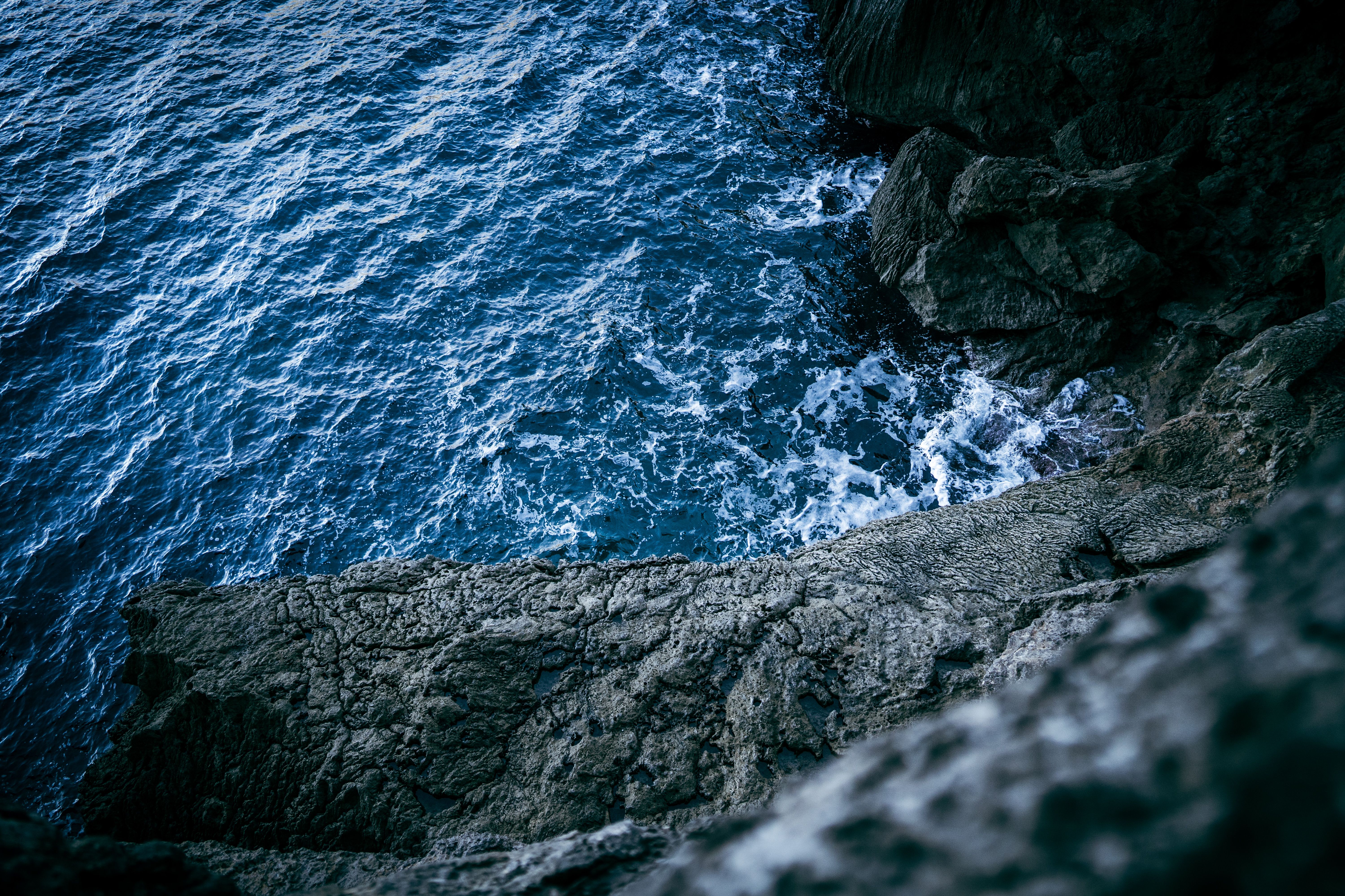 Aerial view of an eroded rocky shoreline with dramatic ocean waves crashing below.
