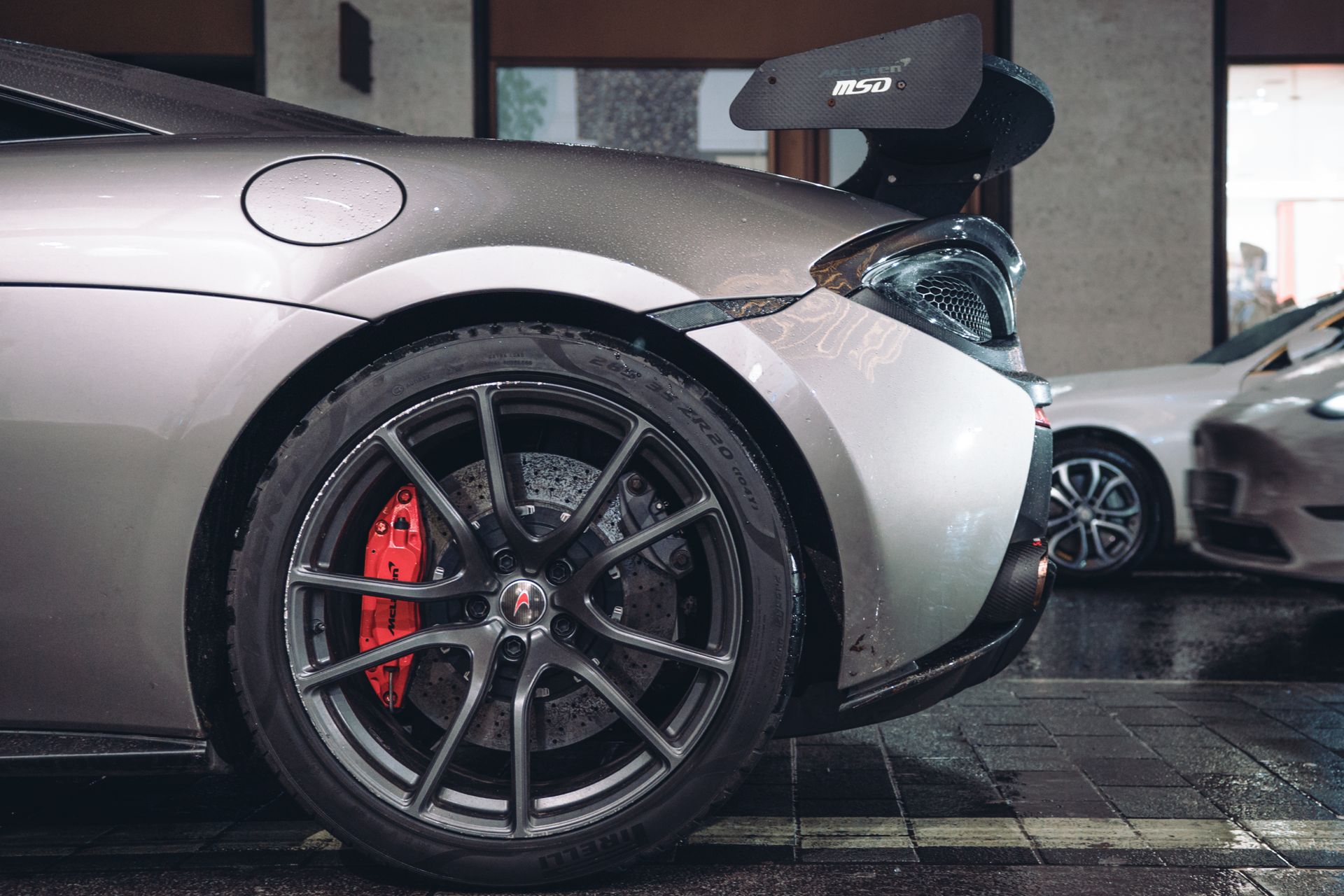 Detailed view of a luxury sports car's wheel and spoiler on a wet city street.