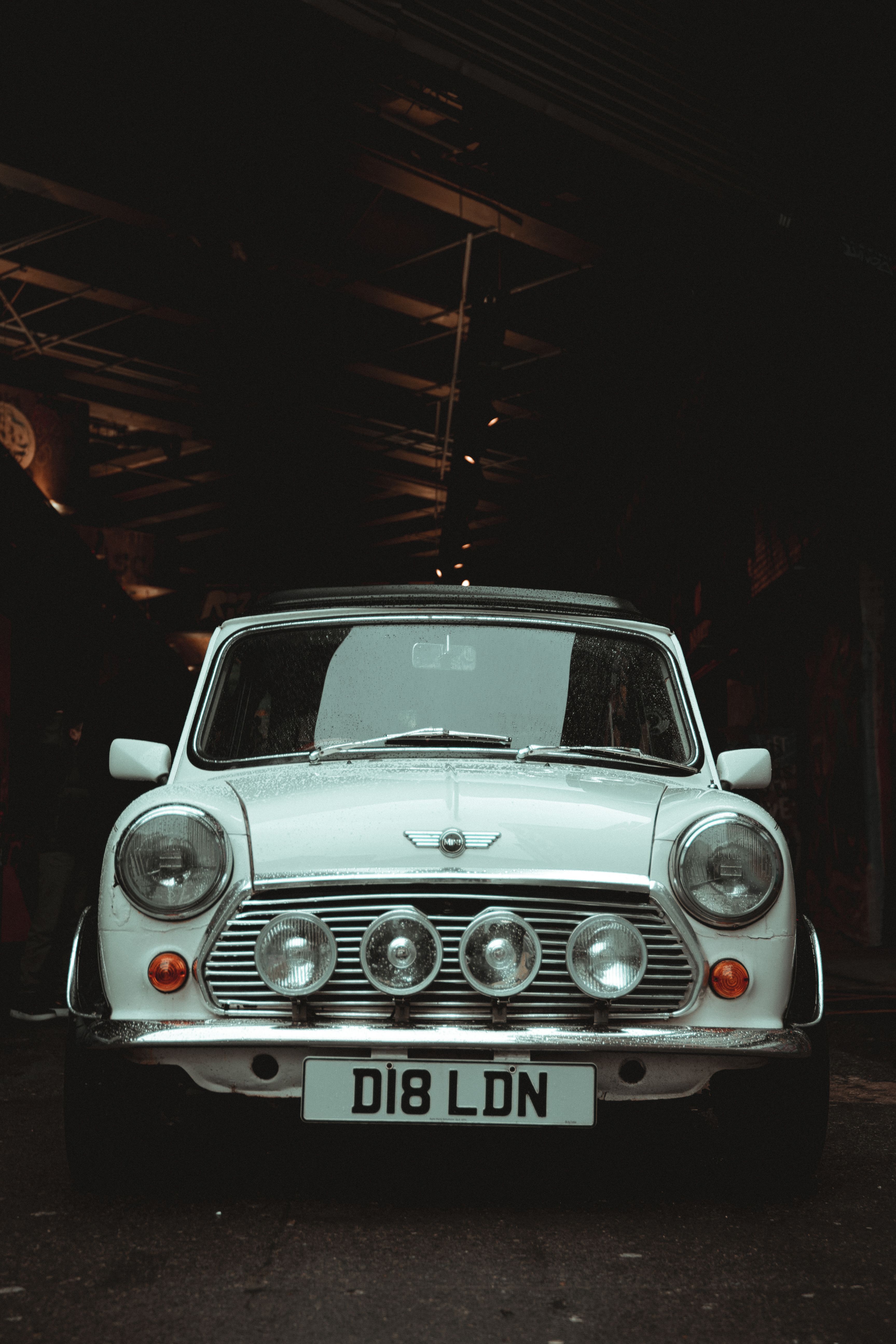 Front view of a vintage white Mini Cooper car with a unique license plate, captured in a dark urban setting.