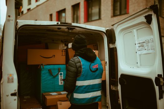 A delivery worker in a reflective vest loads packages into a van in a city setting.