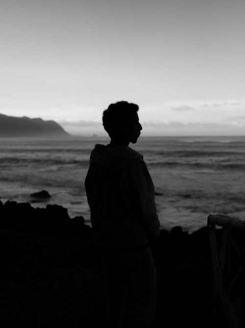 Free Silhouette of an adult standing by the sea during twilight. Dramatic black and white photography captures the serene horizon. Stock Photo