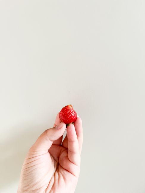 Soft focus image of a hand holding a fresh strawberry against a minimalist background.