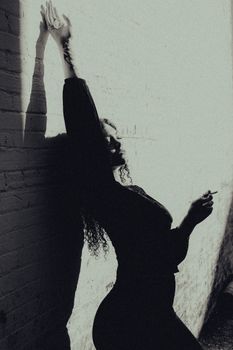Dramatic silhouette of woman in urban setting with strong shadows on wall, black and white.