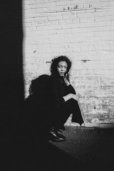 Dramatic black and white photo of a woman squatting against a brick wall.