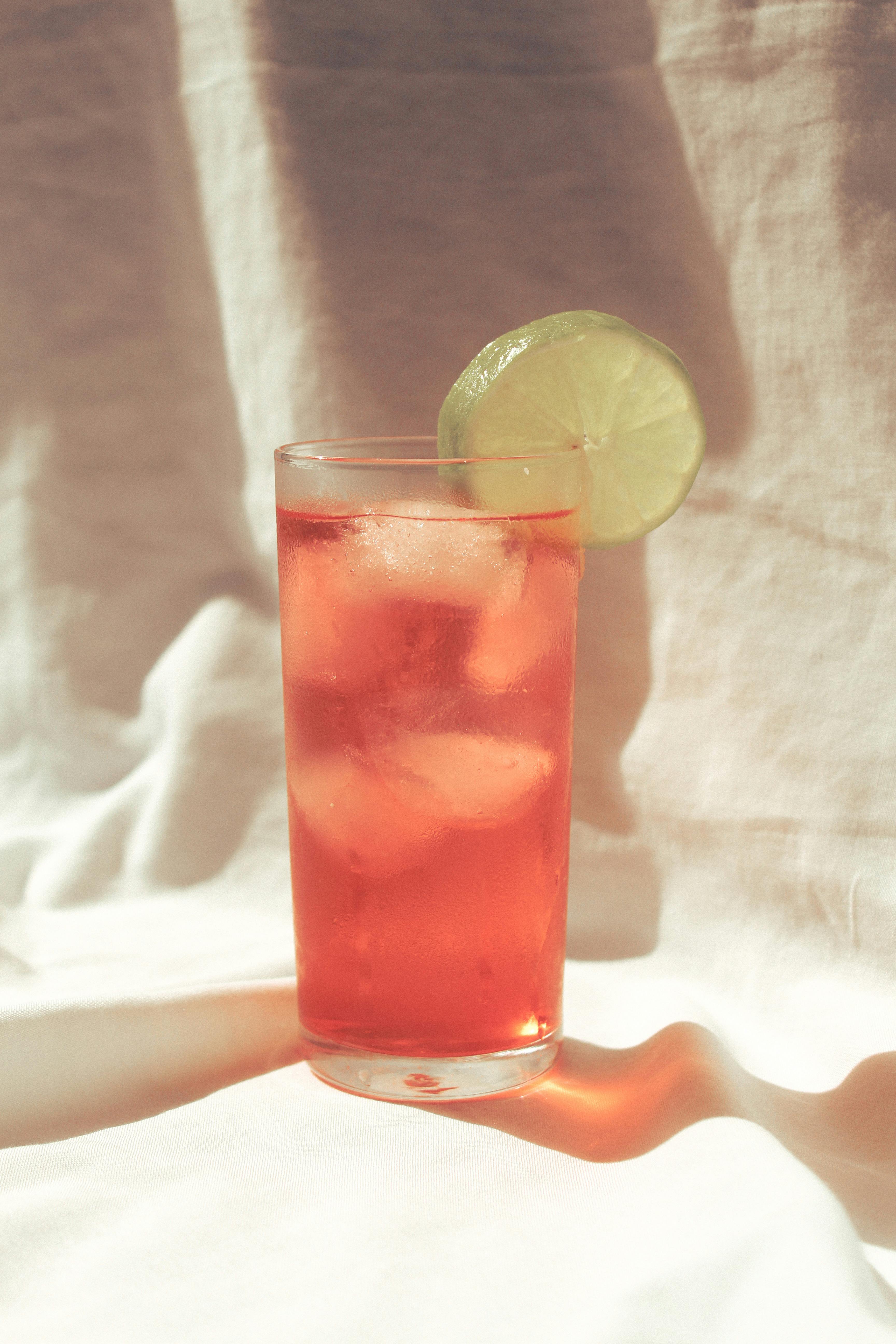 Chilled red cocktail with ice and lime slice on white fabric. Perfect summer refreshment.