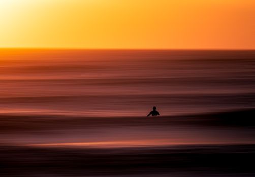 A lone surfer silhouetted against a stunning sunset over the calm ocean waves in Miyazaki, Japan.
