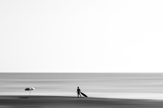 Minimalist black and white photo of a surfer walking on Miyazaki beach with a surfboard.