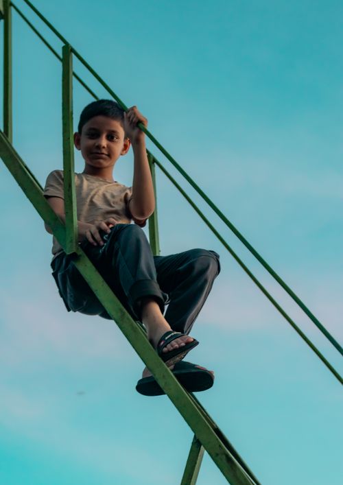 Free A young boy sitting on metal stairs against a bright blue sky in Sylhet, Bangladesh. Stock Photo