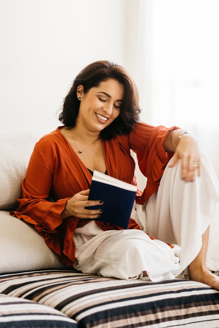 Photo Of Smiling Woman Sitting On A Sofa And Keeping A Book