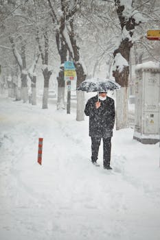 A man walks through snow-covered streets in Malatya, Turkey during winter, using an umbrella for protection.
