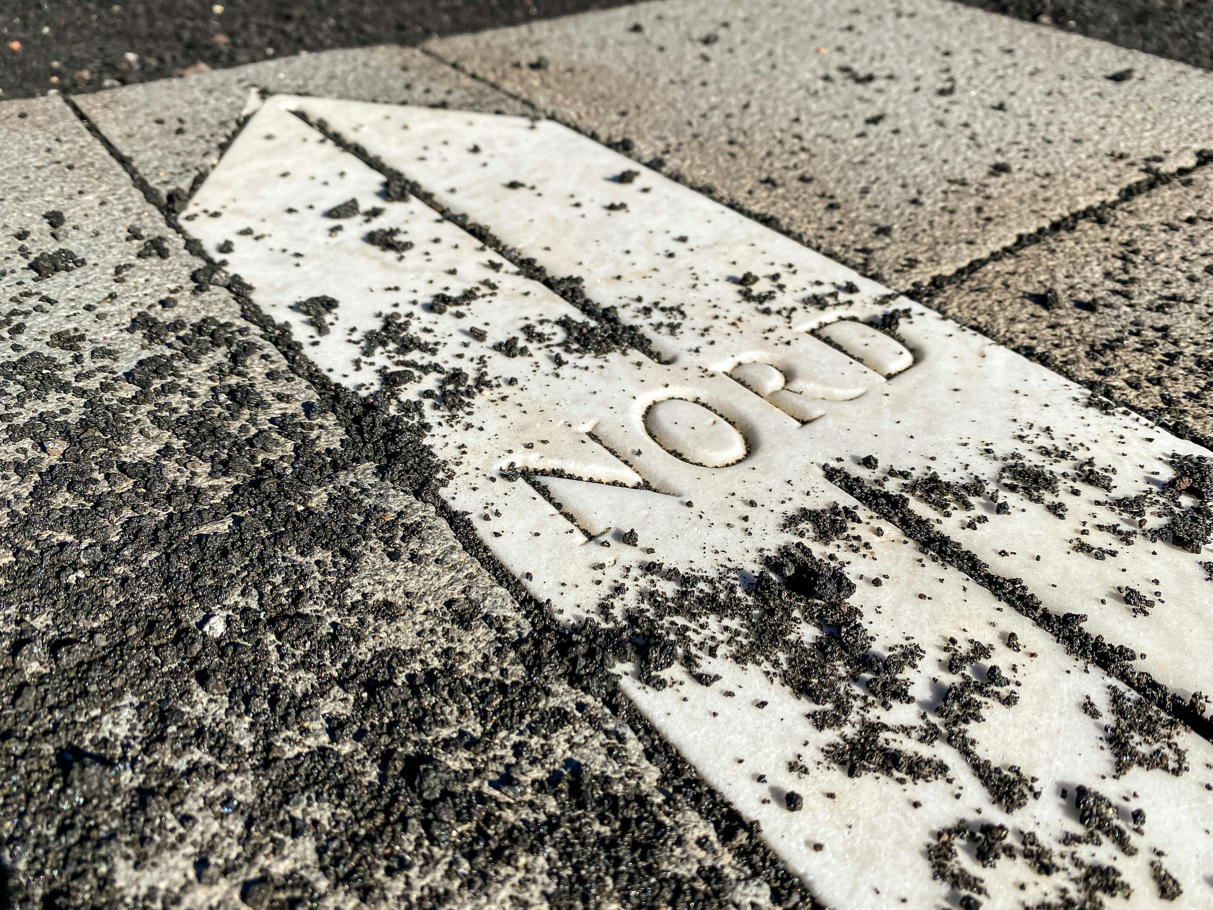 Close-up of a Nord arrow embedded in textured ground indicates direction in Nicolosi, Sicily.
