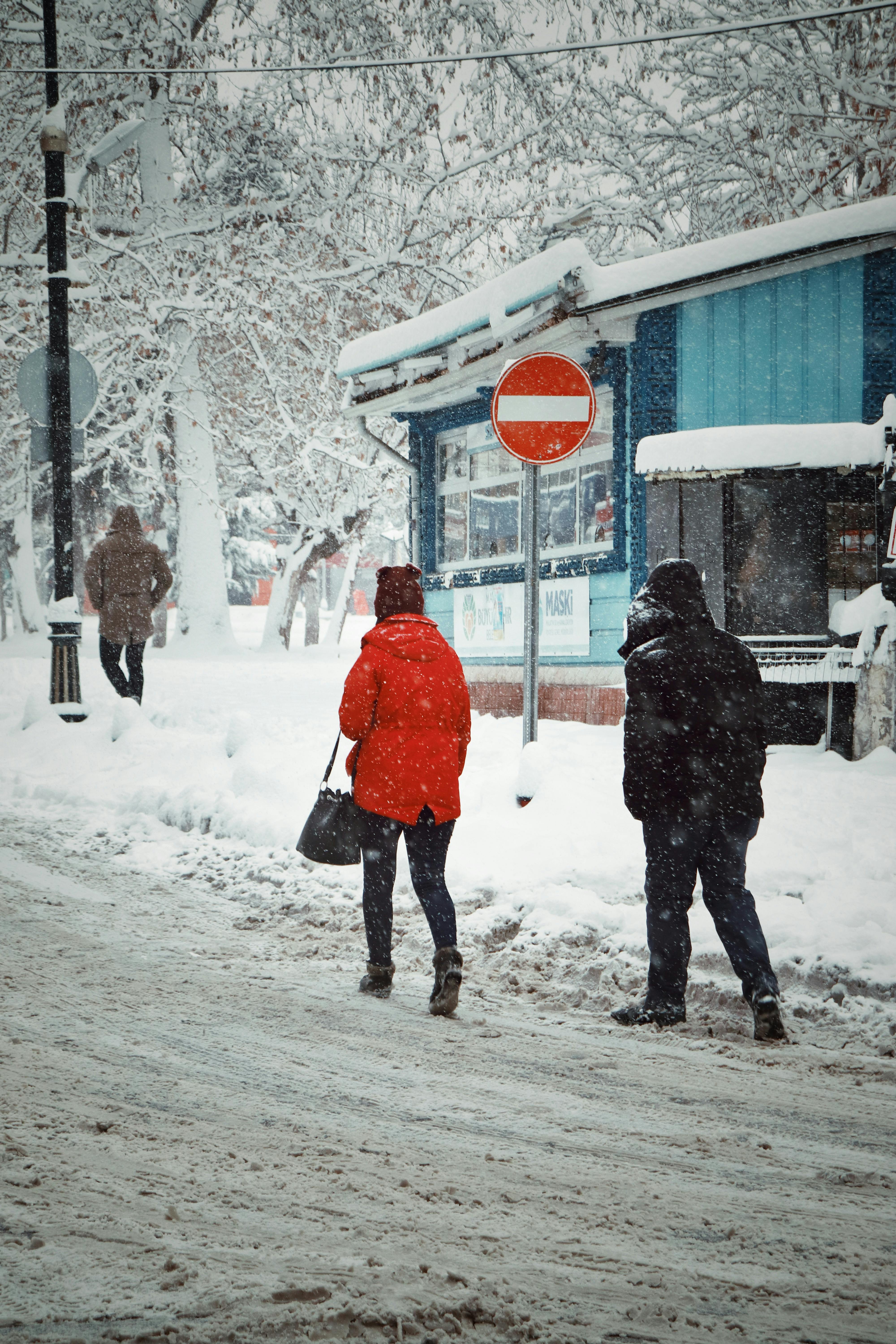 People walking along a snowy street in Malatya, Turkey with snow-covered trees and a no entry sign.