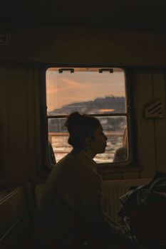 Profile of a woman sitting in a train with a scenic sunset view through the window.