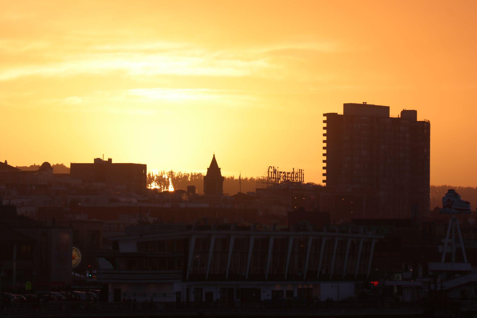 Silhouette of San Francisco cityscape with Ghirardelli sign at sunset.