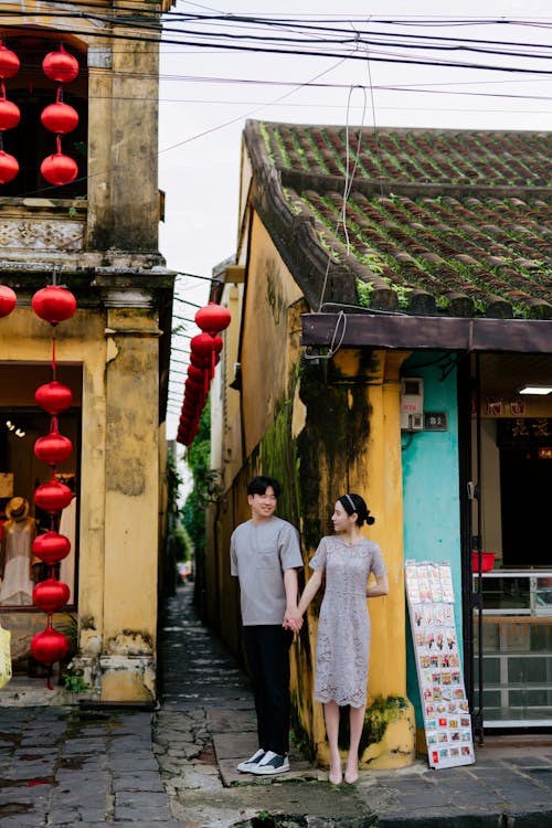 Couple Holding Hands Standing by Narrow Street Decorated with Red Paper Lanterns