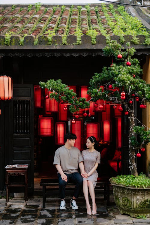 Couple Sitting on Bench under Tree Decorated in Red Ornaments