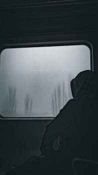 Moody silhouette of a woman in a train gazing out at a rainy landscape in İzmir, Turkey.