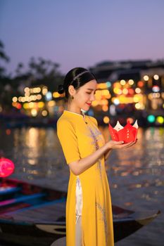 Elegant woman in a yellow dress holding a decorative lantern by a waterway at night.