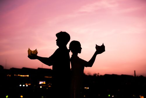 Free A couple silhouetted against a vibrant sunset, holding traditional lanterns symbolizing love and togetherness. Stock Photo
