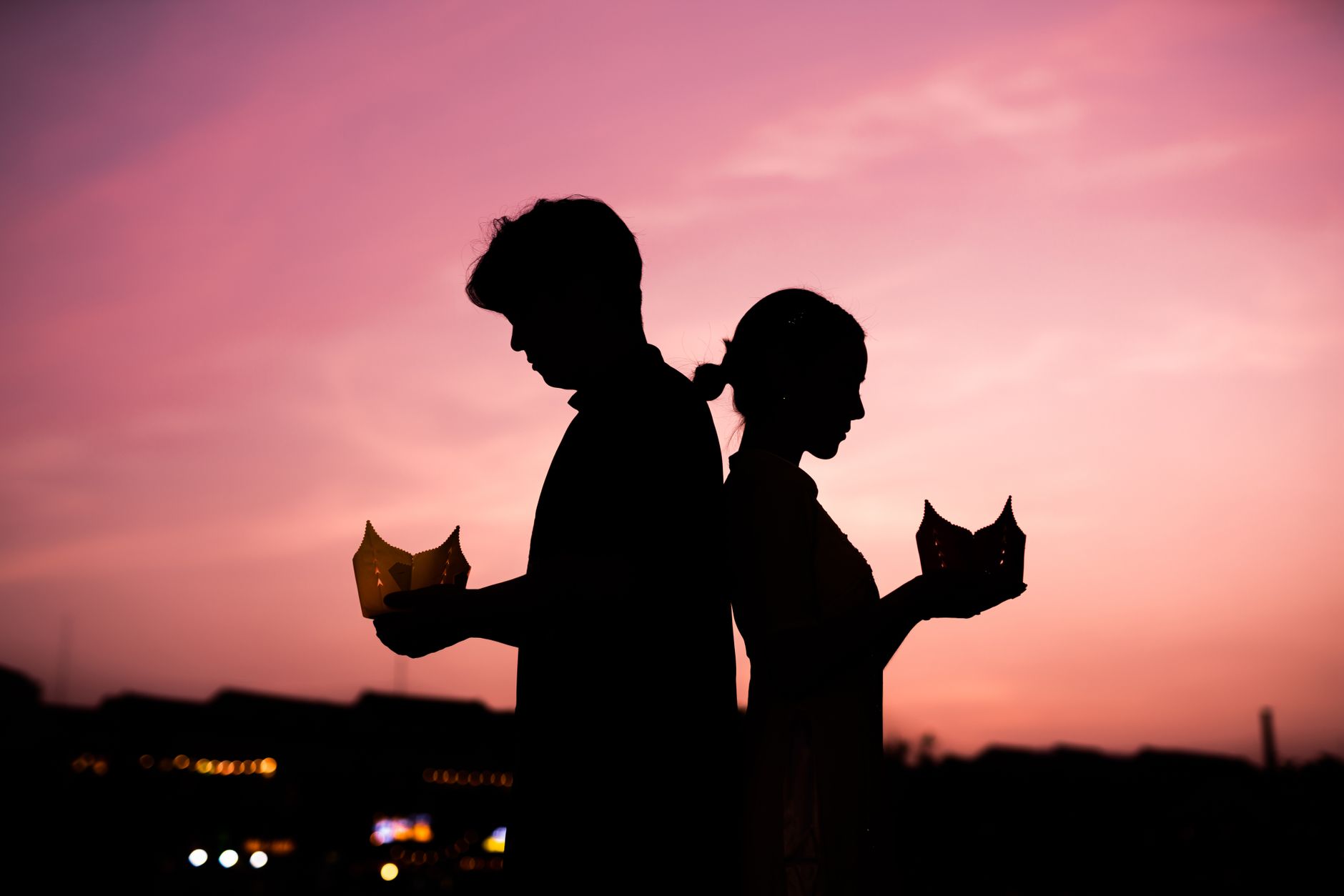 Silhouette of a couple holding lanterns, symbolizing romance against a vibrant sunset sky.
