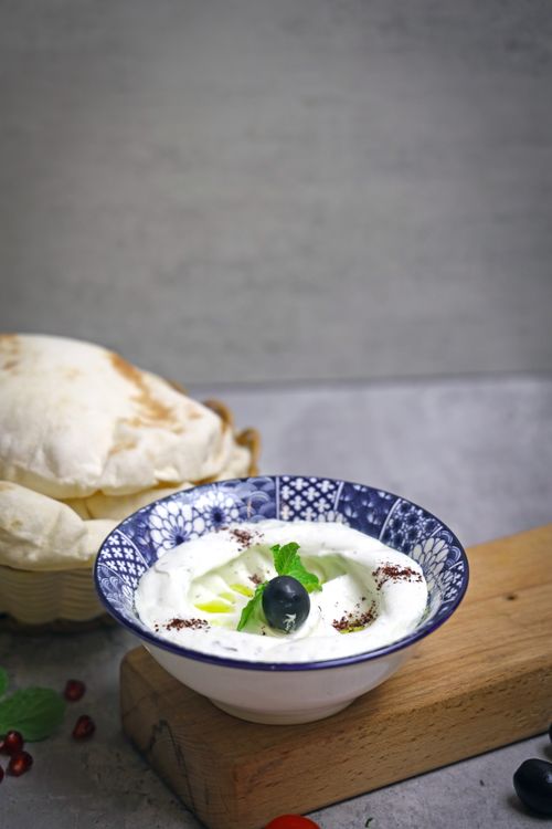Free Delicious fresh tzatziki sauce garnished with mint and berries in an ornate blue bowl on wooden board. Stock Photo