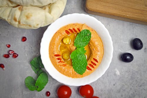 A bowl of hummus with pomegranate, mint and olives