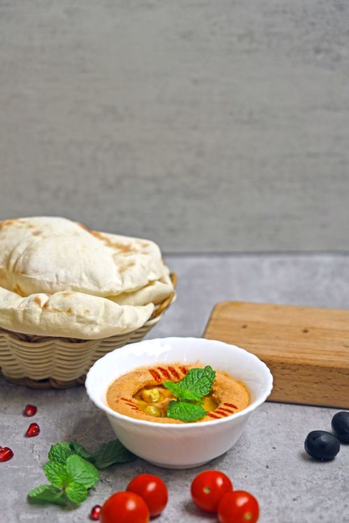 Free Delicious Middle Eastern hummus served with pita bread, fresh tomatoes, and mint leaves on a rustic table. Stock Photo