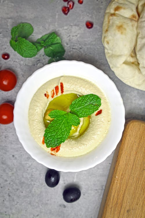 A bowl of hummus with pomegranate, mint and olives