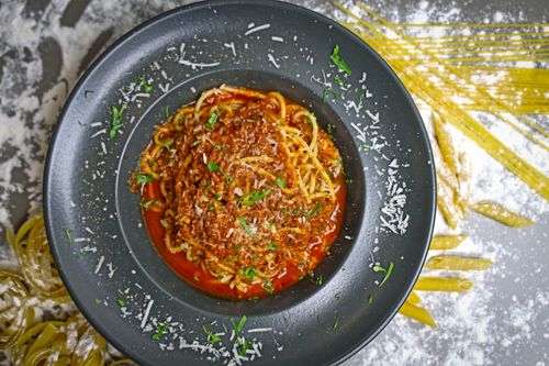 Free A close-up of a flavorful spaghetti bolognese topped with Parmesan cheese on a dark plate. Stock Photo