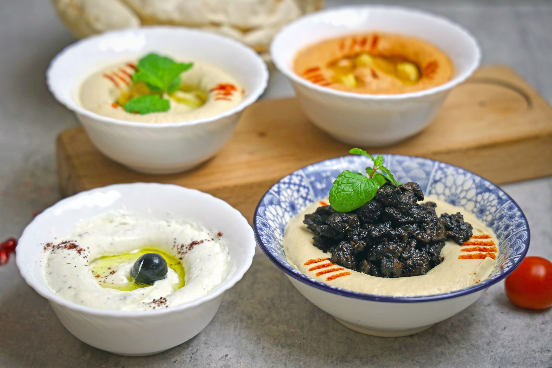 Three bowls of hummus with olives and black olives