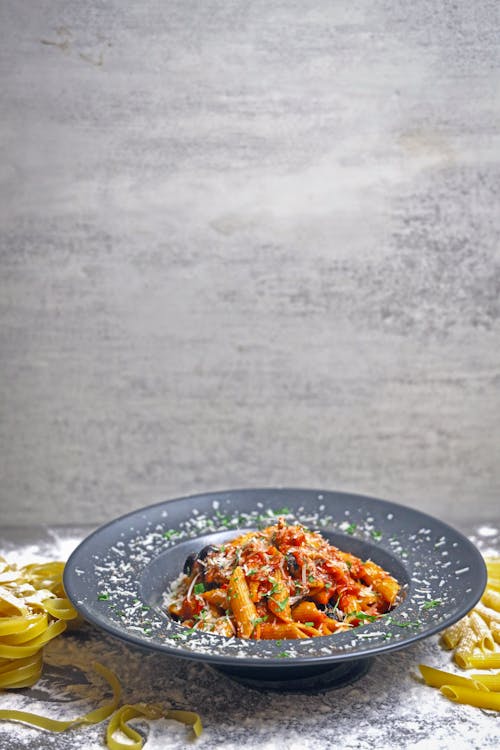 A black plate with pasta and sauce on it