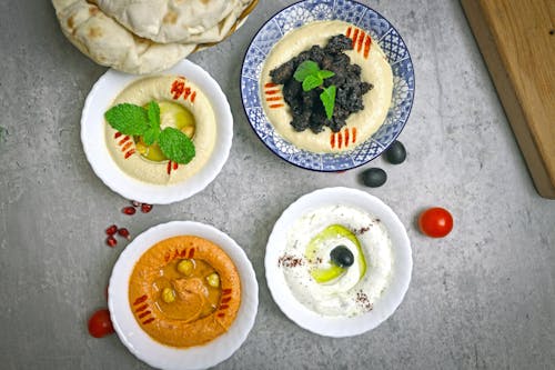 A table with four bowls of hummus and a bowl of olives