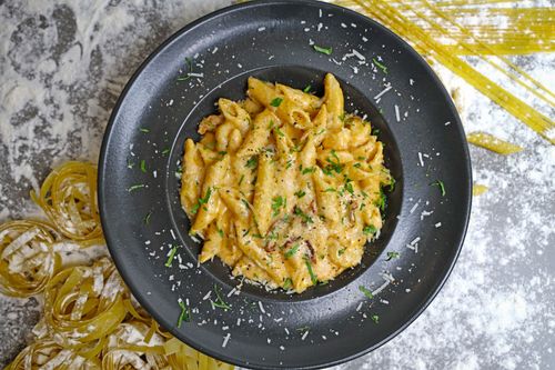 Free Top view of creamy penne pasta garnished with herbs and cheese, served on a dark plate. Stock Photo