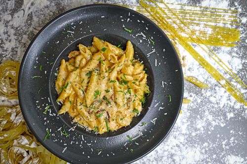 Free Delicious creamy penne pasta garnished with herbs in a stylish black bowl. Stock Photo