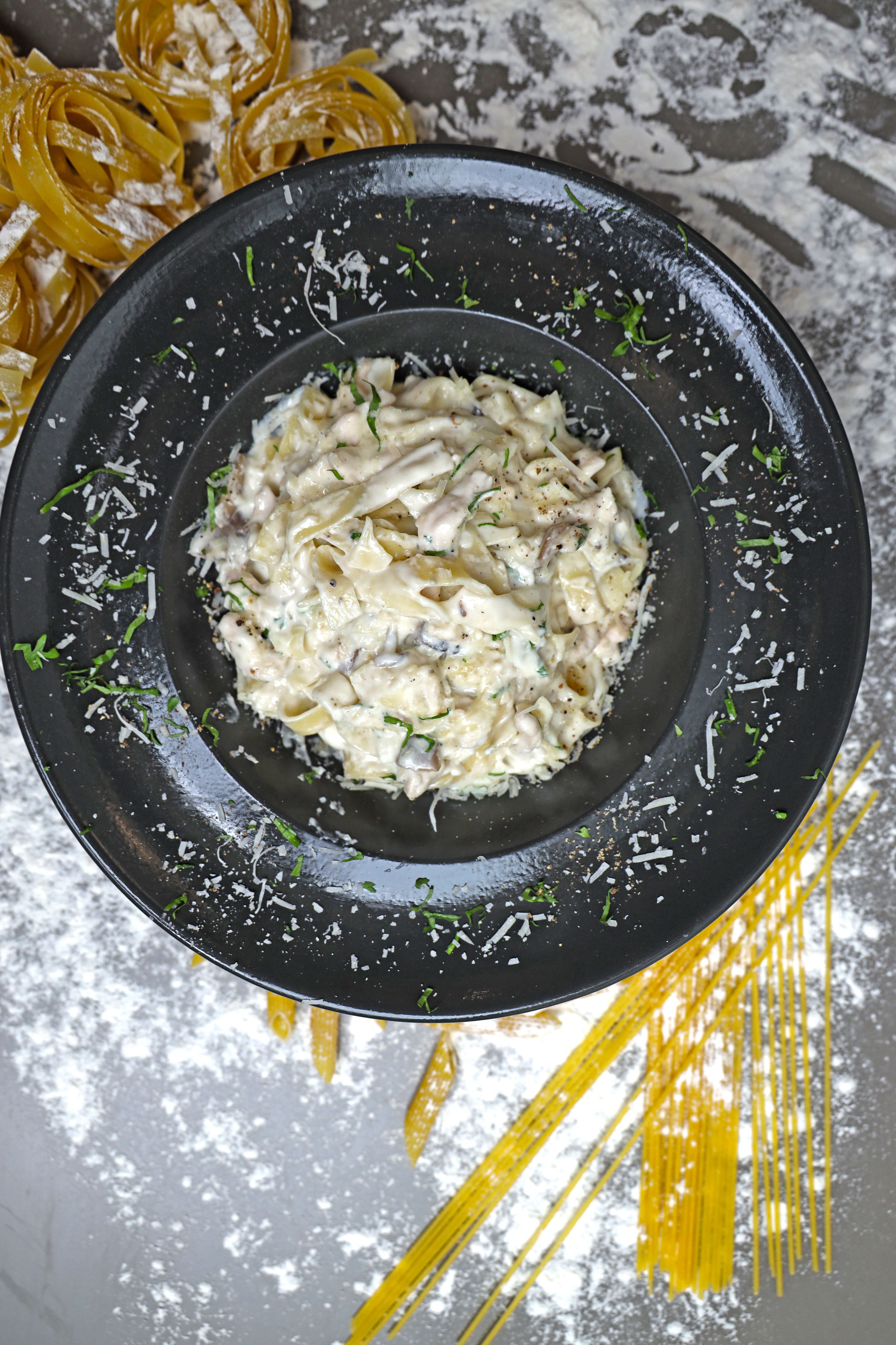 Top view of creamy fettuccine Alfredo garnished with Parmesan cheese and herbs on a black plate.