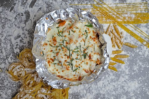 A foil pan with pasta and cheese on top