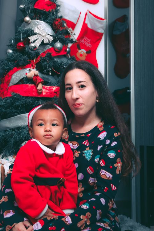 Free Festive portrait of a mother and child in holiday attire by a Christmas tree indoors. Stock Photo