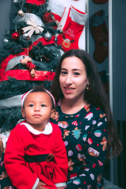Free A mother and her child in festive outfits beside a Christmas tree, enjoying holiday cheer. Stock Photo