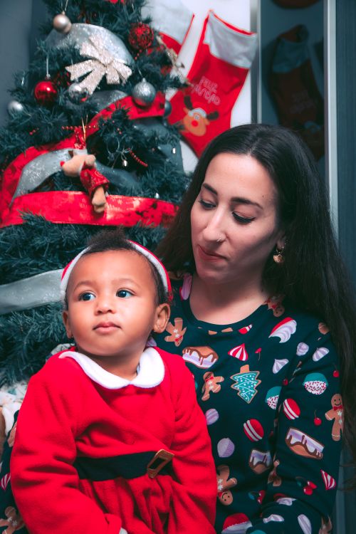 Free Mother and child in holiday attire in front of a decorated Christmas tree. Stock Photo