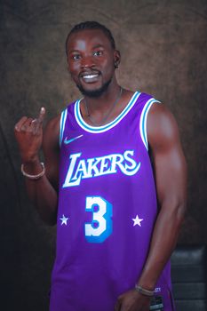 Cheerful man in Lakers jersey smiling confidently in studio shot.