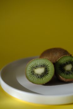 Vibrant kiwi slices displayed on a white plate with a contrasting yellow background, perfect for healthy food concepts.