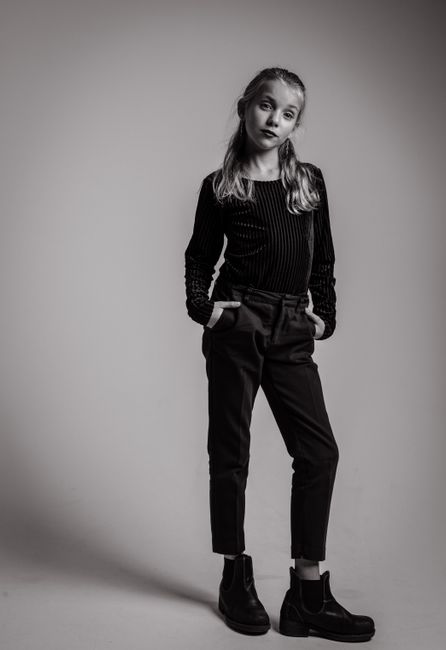 A black and white portrait of a young girl posing confidently in stylish attire, showcasing elegance and attitude.